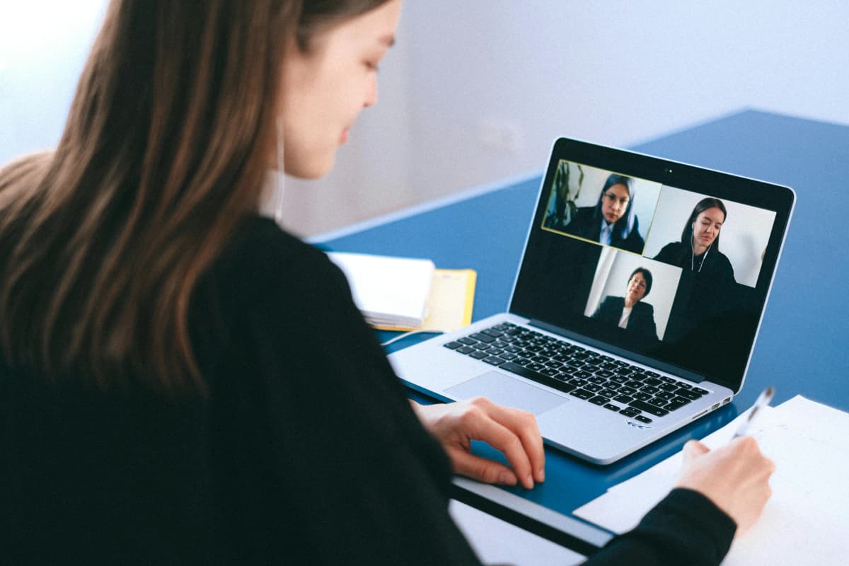 Joven estudiante tomando un curso grupal en línea interactuando con sus compañeras en su laptop
