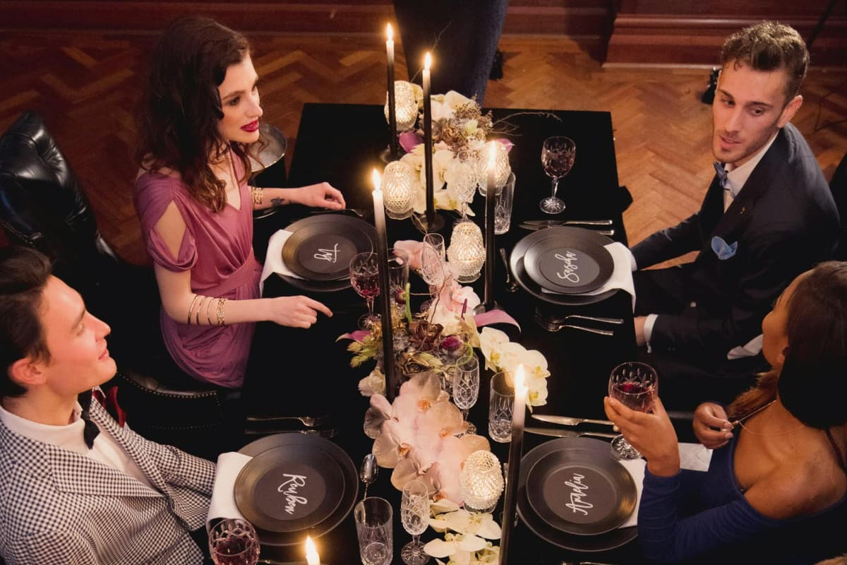 Dos parejas conversando durente un evento de cena formal en mesa decorada y con velas en un restaurante de lujo