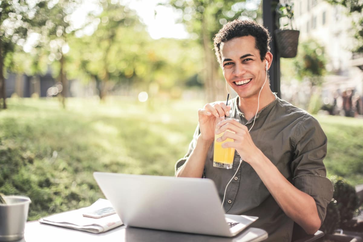 Estudiante practicando el inglés en línea en un jardín mientras disfruta una bebida